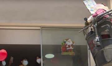 En escalera de bomberos, Papá Noel entrega regalos a niños internados con COVID-19
